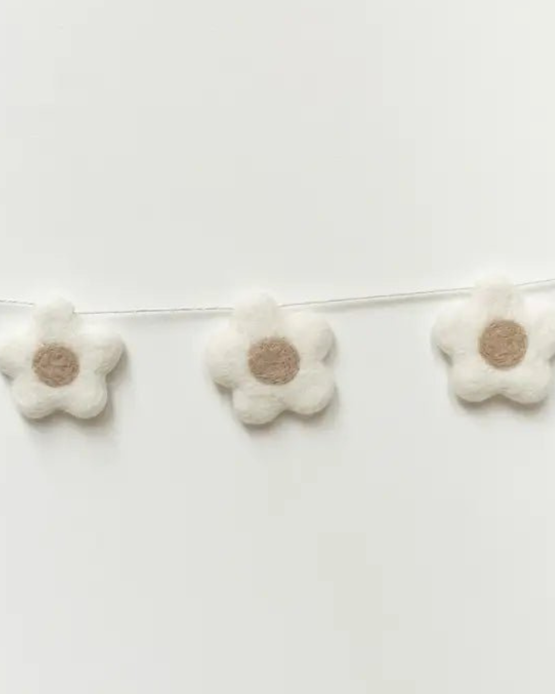 Gros plan sur les fleurs en laine feutrée de la guirlande décorative pour chambre de bébé.