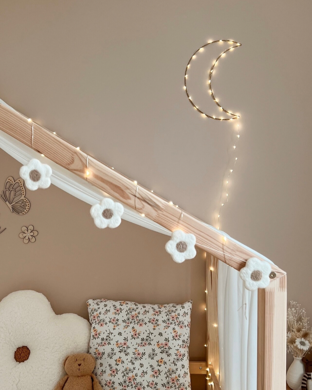 Guirlande de fleurs en laine feutrée décorant un lit cabane dans une chambre de bébé au style bohème.